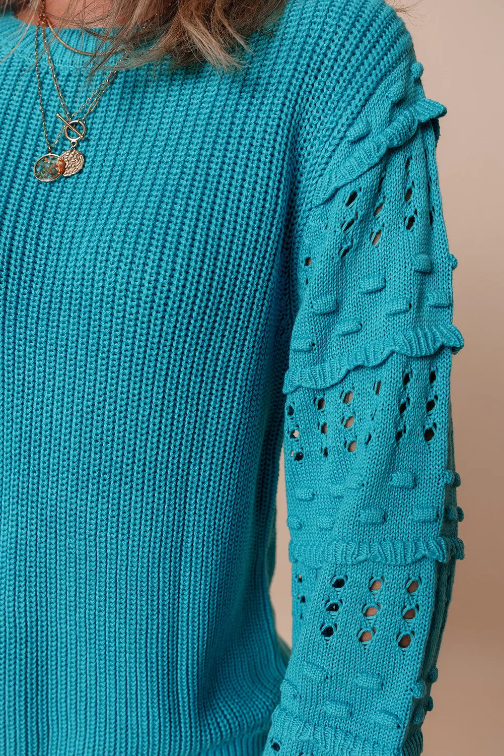 Turquoise knit sweater with textured cutout sleeves and ruffled details.