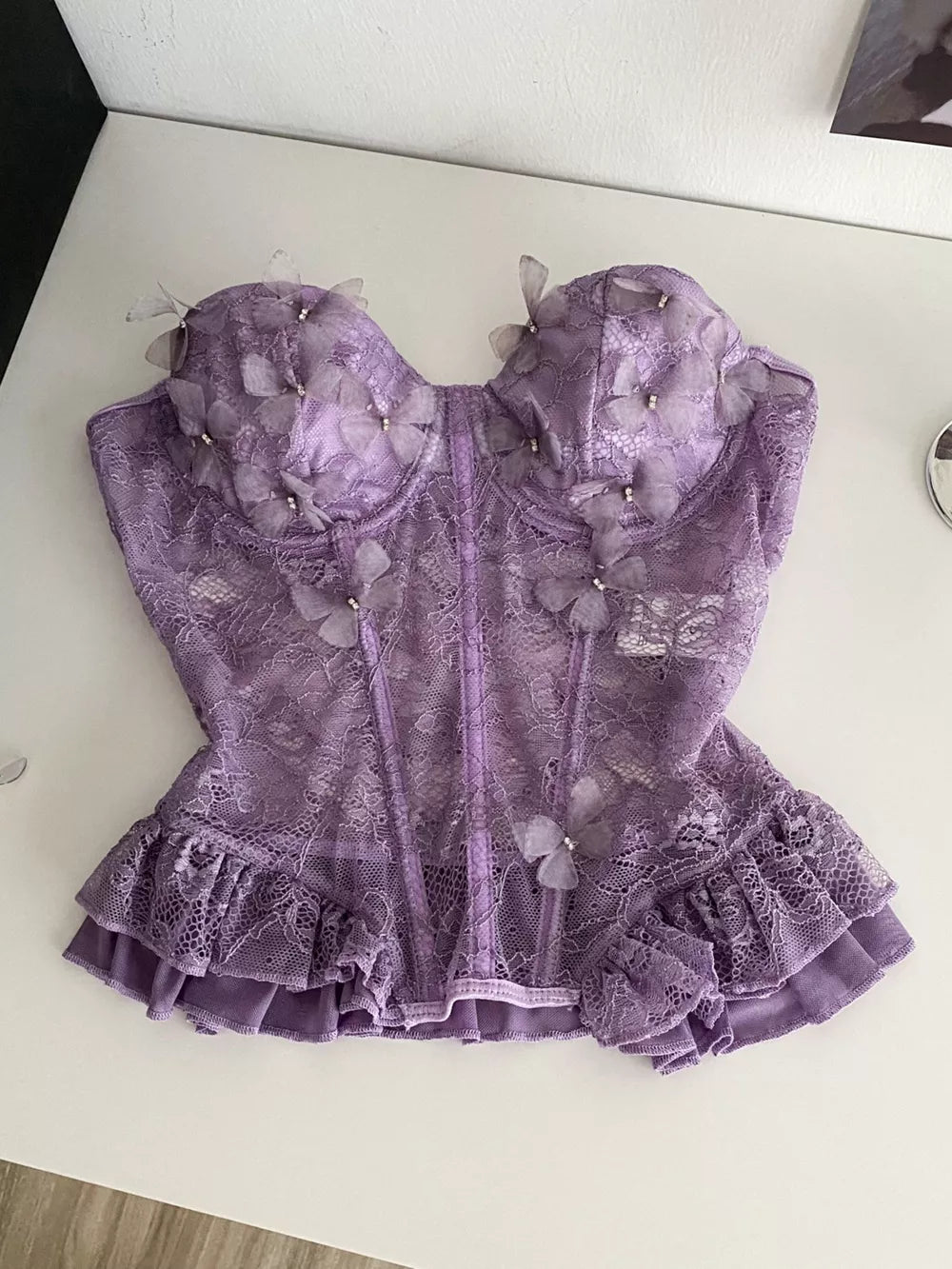 Purple lace bustier top with 3D butterflies, pearl accents, and ruffled hem.