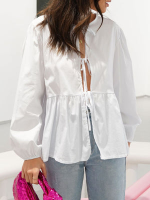 White tie-front peplum blouse with voluminous sleeves and a ruffled hem.