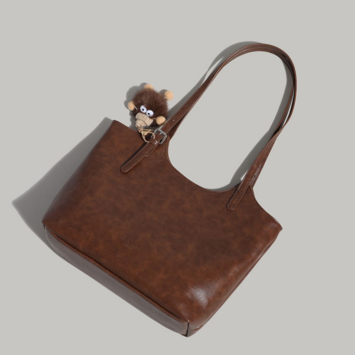Brown pu leather tote bag with a fuzzy charm and adjustable straps.