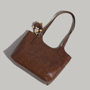 Brown pu leather tote bag with a fuzzy charm and adjustable straps.
