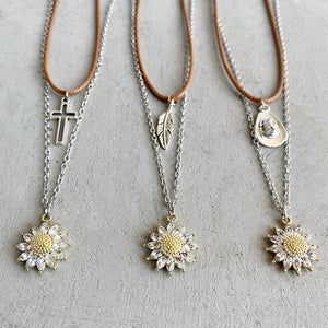 Layered sunflower charm necklaces with cross, feather, and cowboy hat pendants.