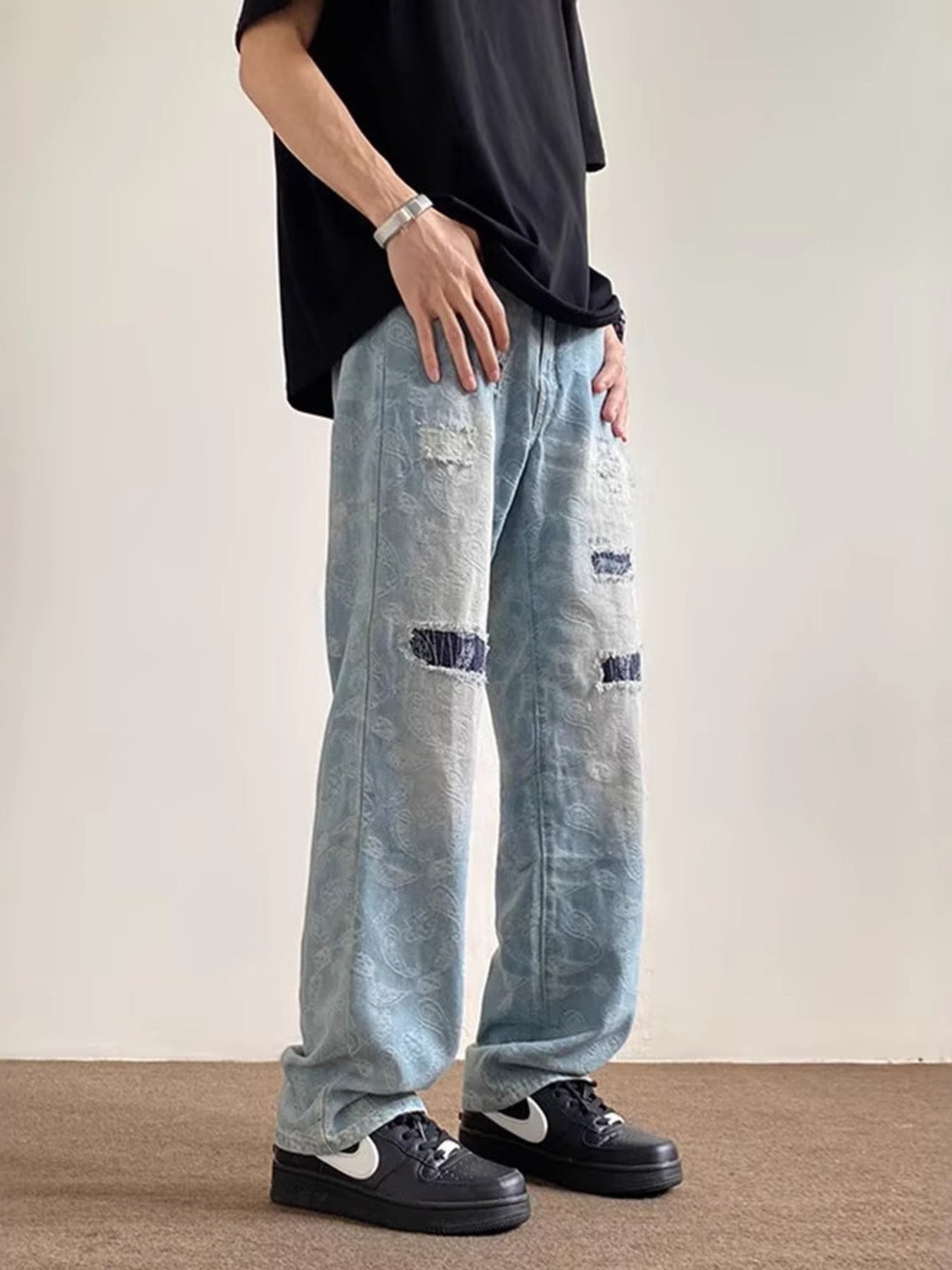 Men's light blue distressed wide-leg jeans with paisley pattern and pocket details.