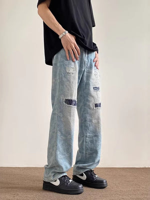 Men's light blue distressed wide-leg jeans with paisley pattern and pocket details.