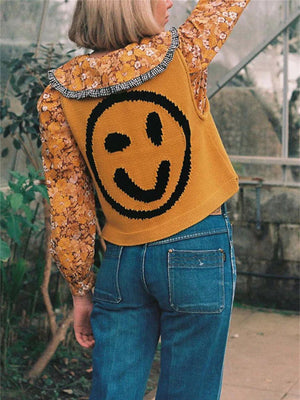 Mustard knit tank top with black smiley face graphic, layered over floral print shirt.