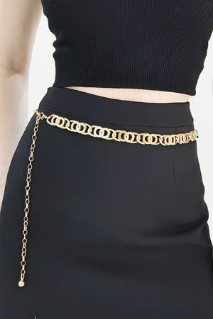 Golden circle chain belt with a long dangling chain and a small charm, worn with a black top and skirt.