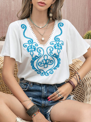 White embroidered medallion blouse with flutter sleeves and V-neckline.