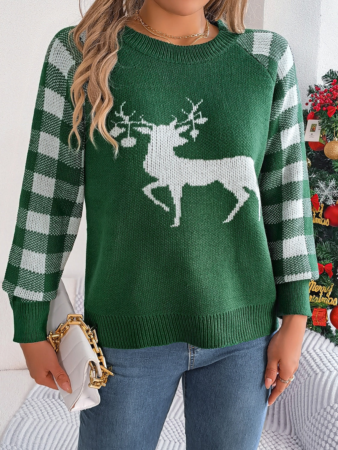 Green crewneck sweater with white reindeer graphic and plaid sleeves.