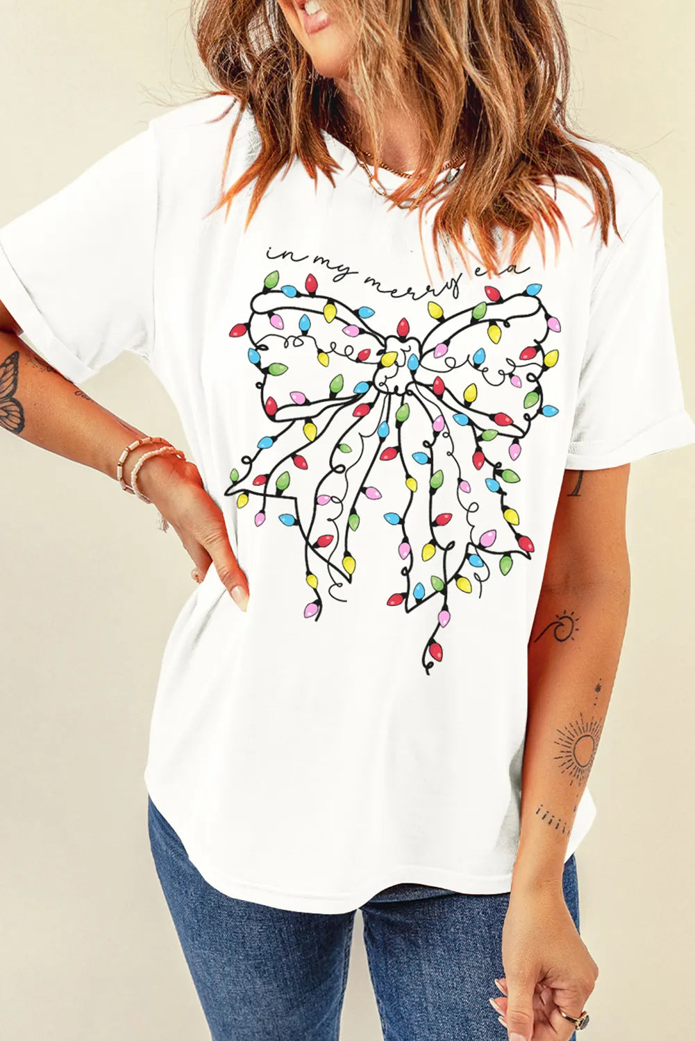 White t-shirt with a colorful holiday light bow graphic and "in my merry era" text.