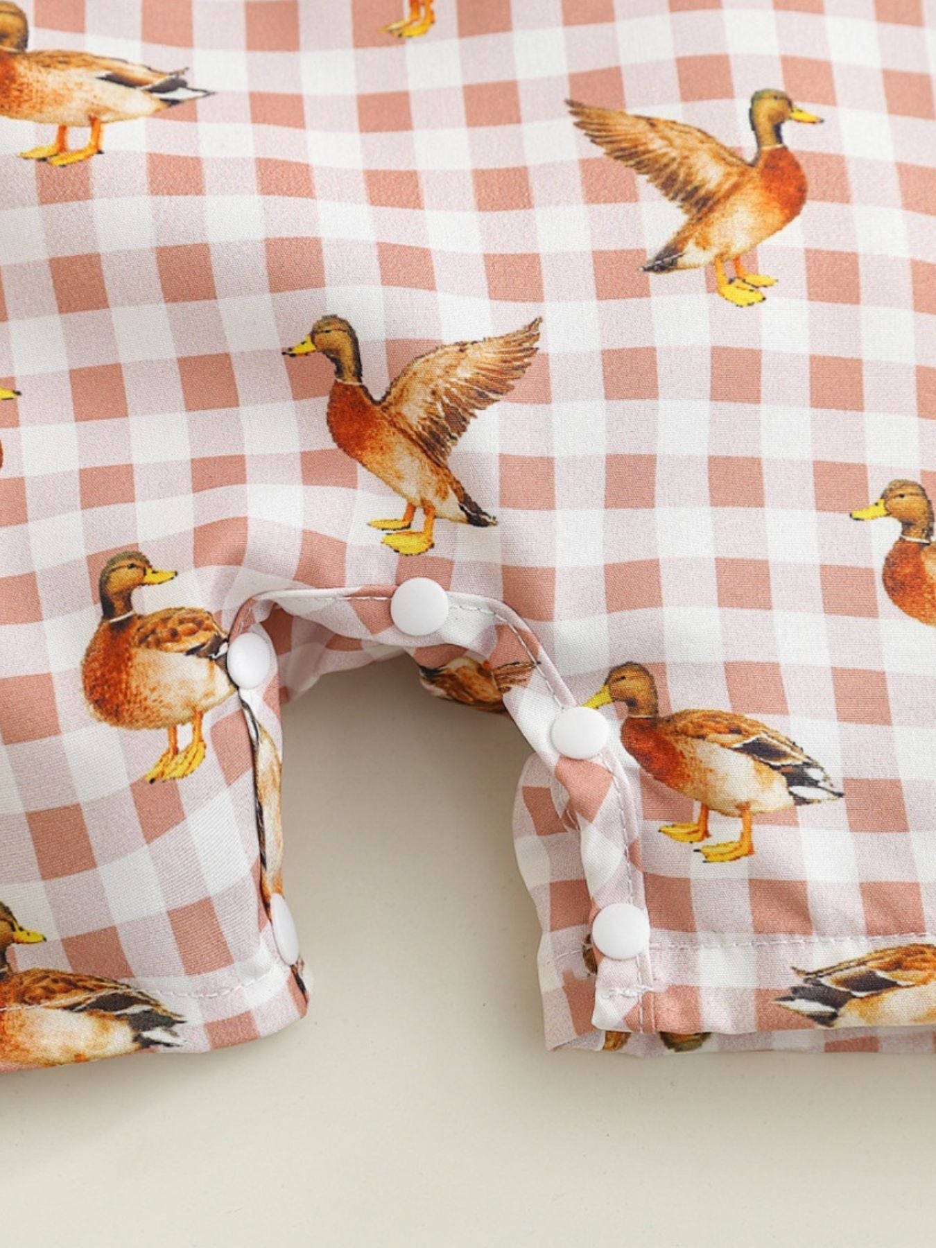 Baby one-piece with duck print on pink gingham, cotton blend fabric, button detail.