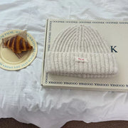 Cozy chunky knit beanie hat in Milky White with a decorative tag.
