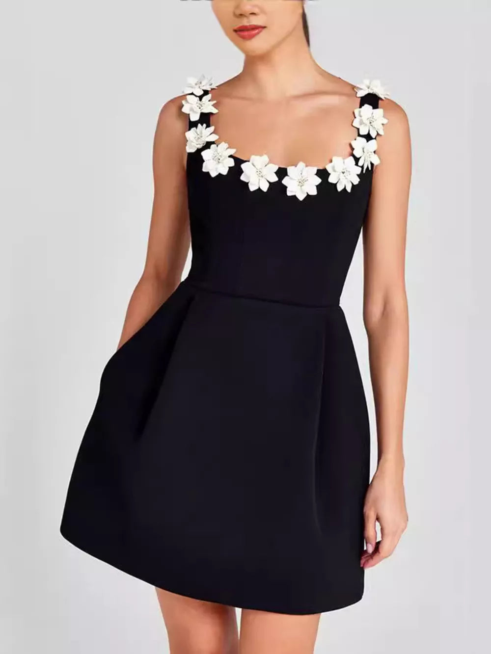 Black mini dress with floral embellishments on straps and square neckline, featuring pockets.