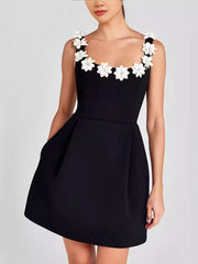Black mini dress with floral embellishments on straps and square neckline, featuring pockets.