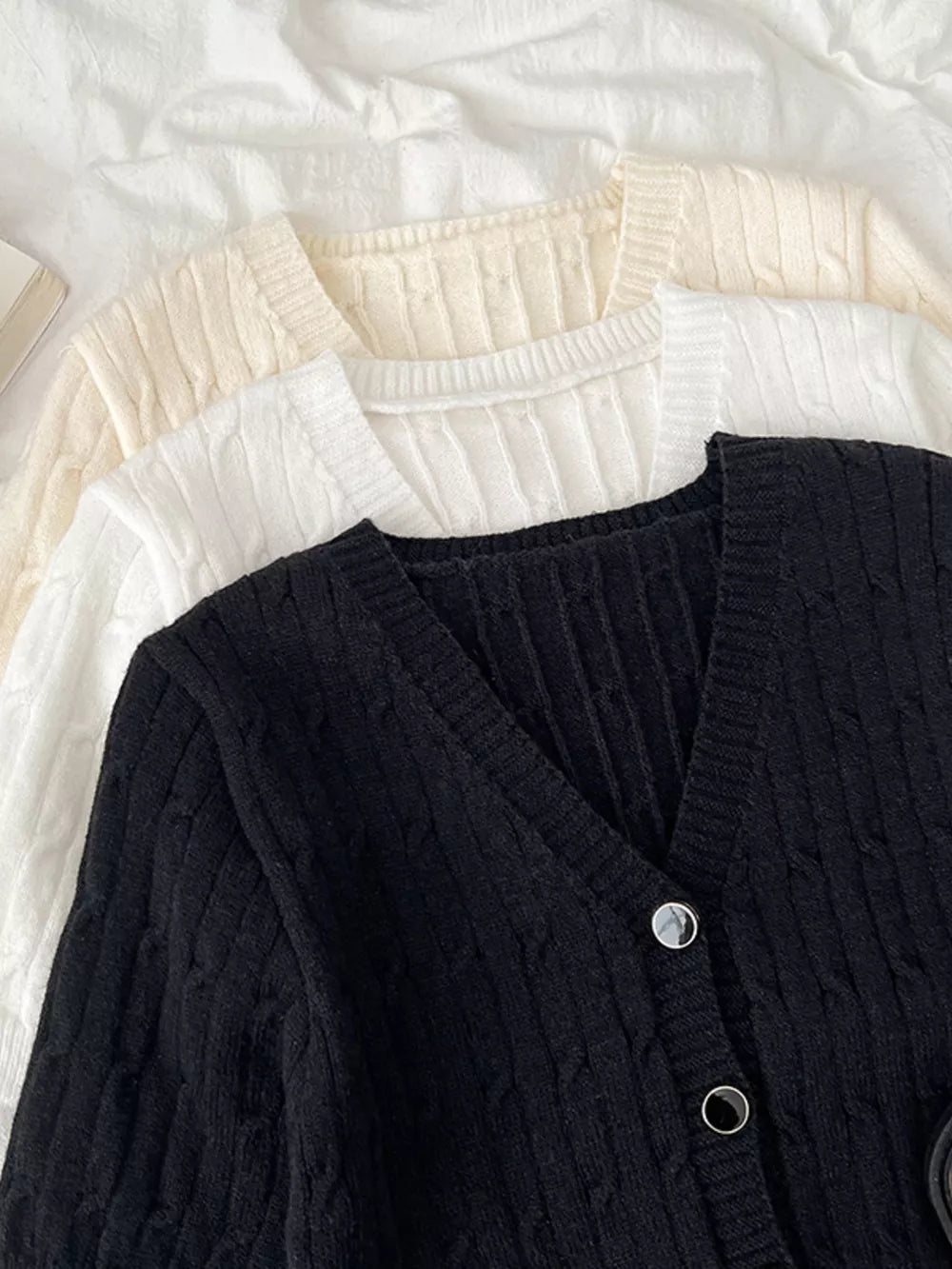 Black cable-knit cropped cardigan with V-neck and button details.