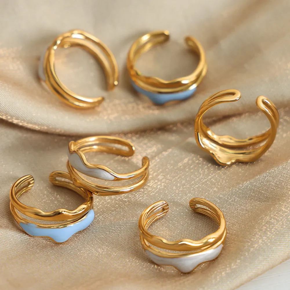 Sculpted enamel wave rings in gold with light blue and white accents.