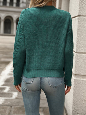 Turquoise cable knit sweater with textured sleeves and crew neck, styled with jeans.