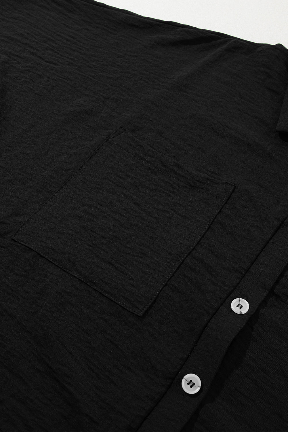 Black oversized shirt romper with textured fabric, button front, and chest pocket.