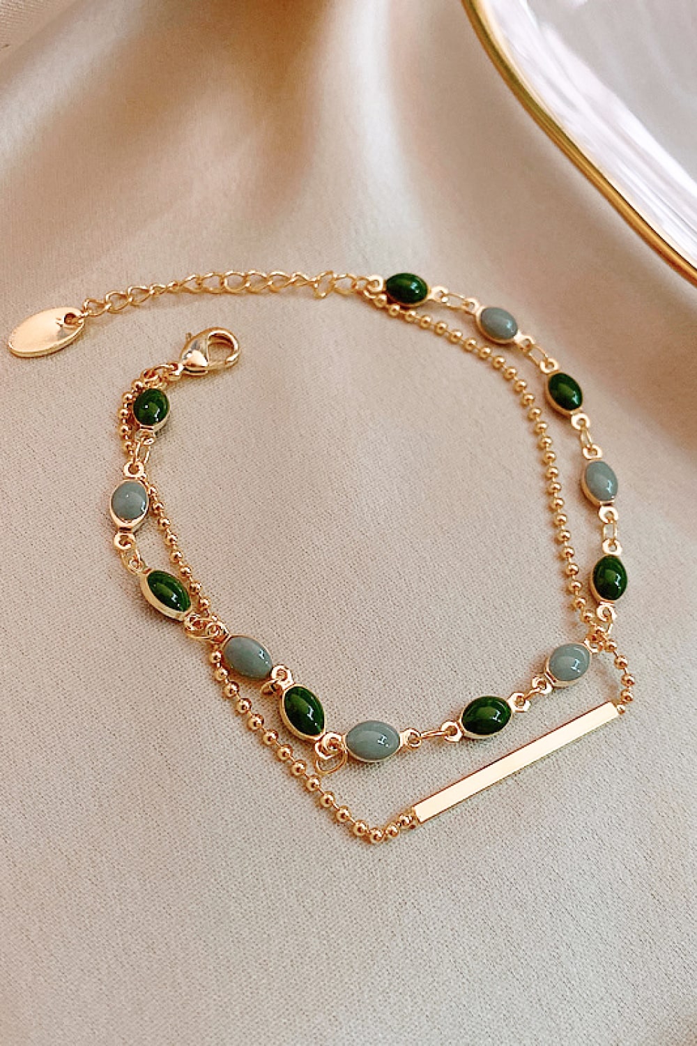 Dual chain gold bracelet with green and grey oval stones and a gold bar accent.