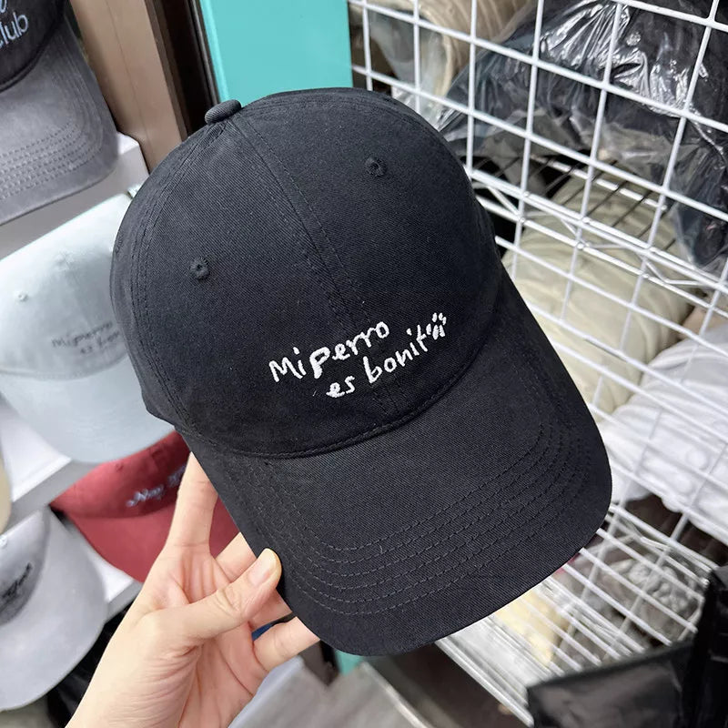 Black baseball cap with "Mi perro es boniti" embroidery and paw print detail.