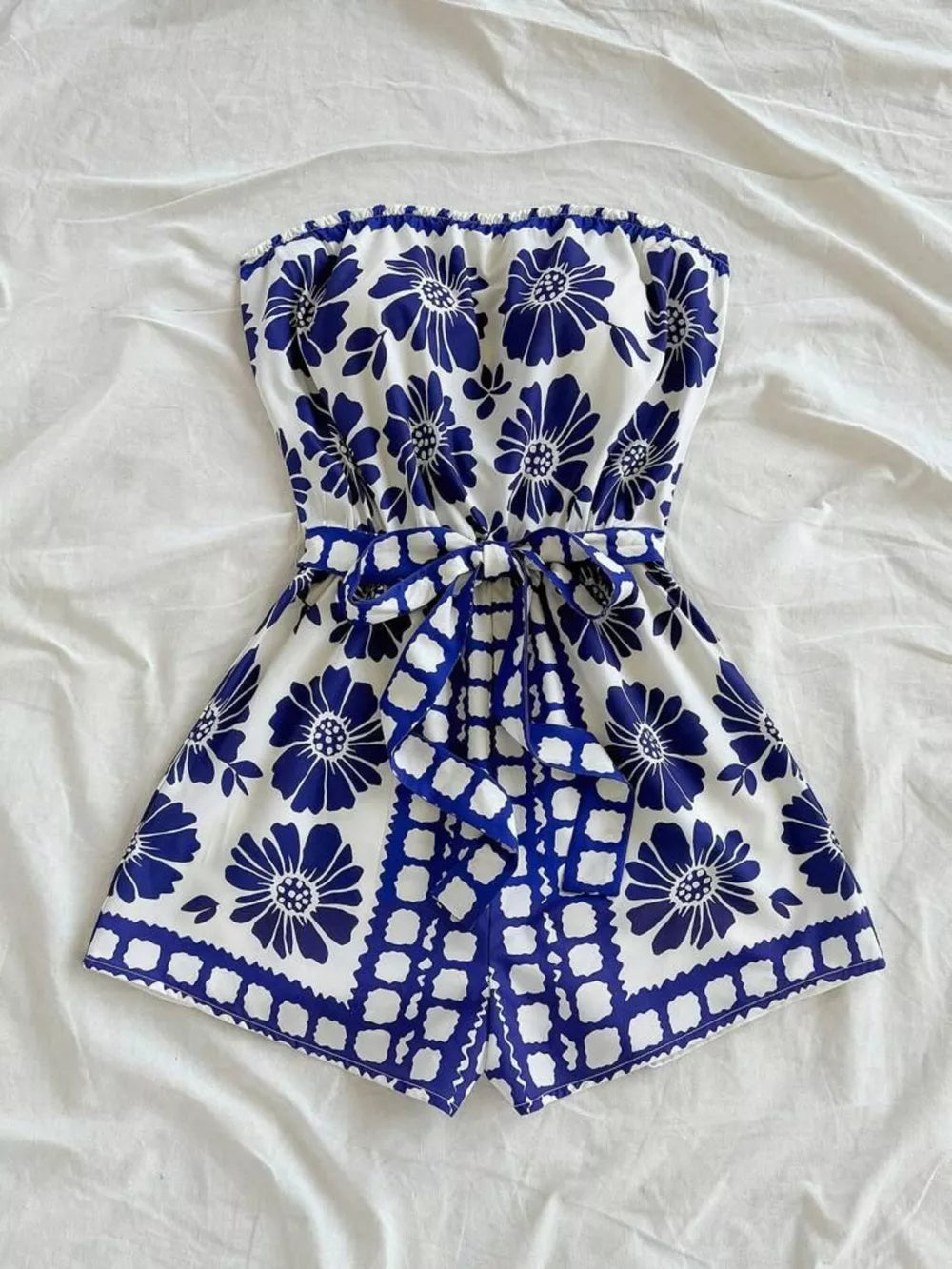 Blue floral tie-waist strapless romper with ruffled hem and tie detail.