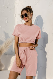 Blush pink loungewear set with rolled sleeve crop top and drawstring shorts.