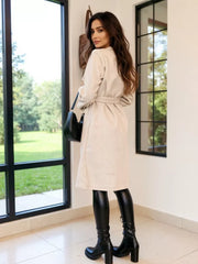 Apricot tailored double-breasted trench coat with waist tie, textured fabric, midi length.