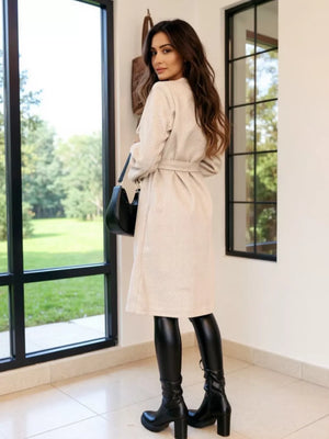 Apricot tailored double-breasted trench coat with waist tie, textured fabric, midi length.