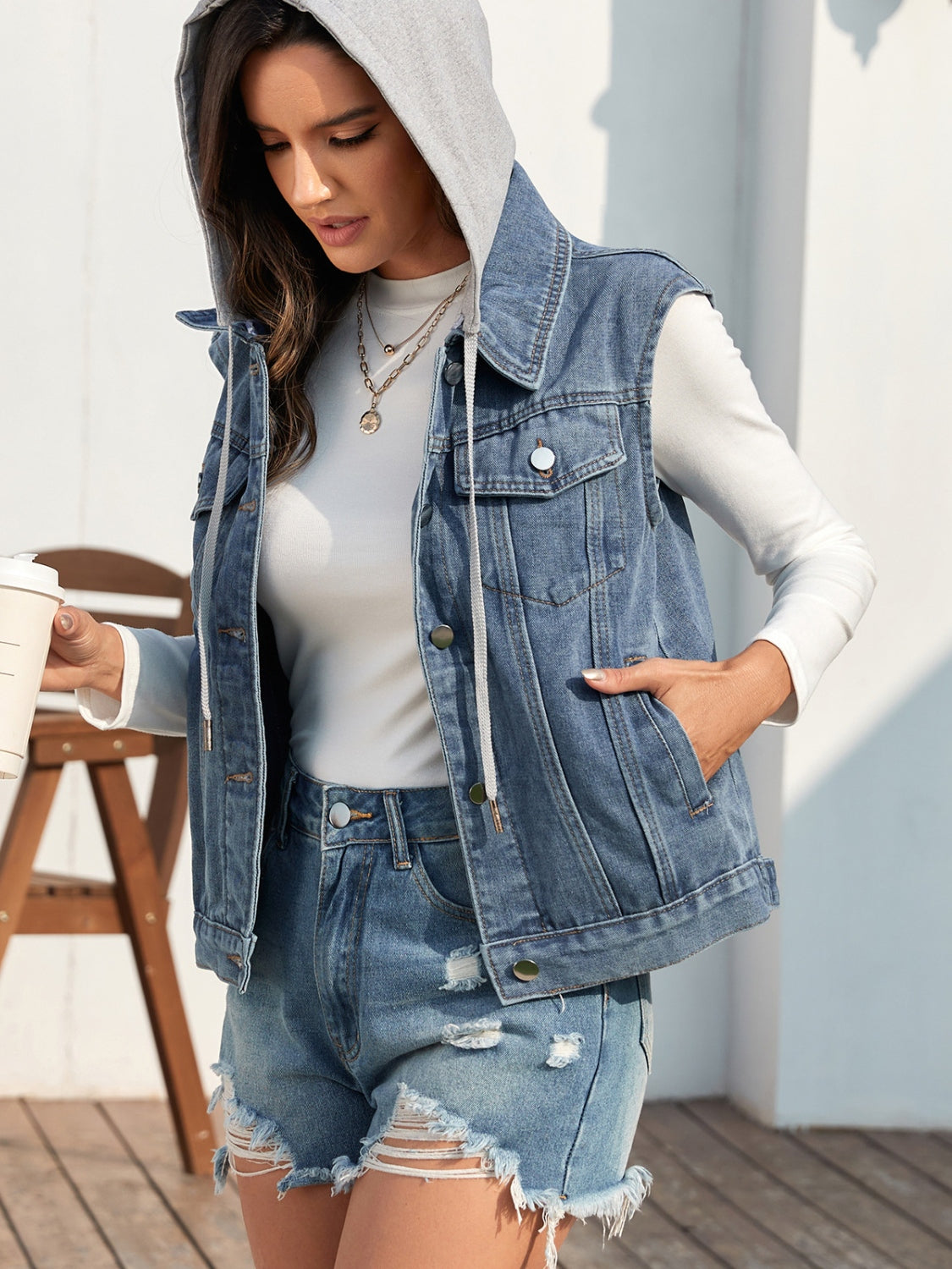 Sleeveless denim vest in medium blue with attached grey hood and button front.