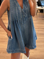 Light blue denim playsuit with V-neck, tie front, and vertical pleats.