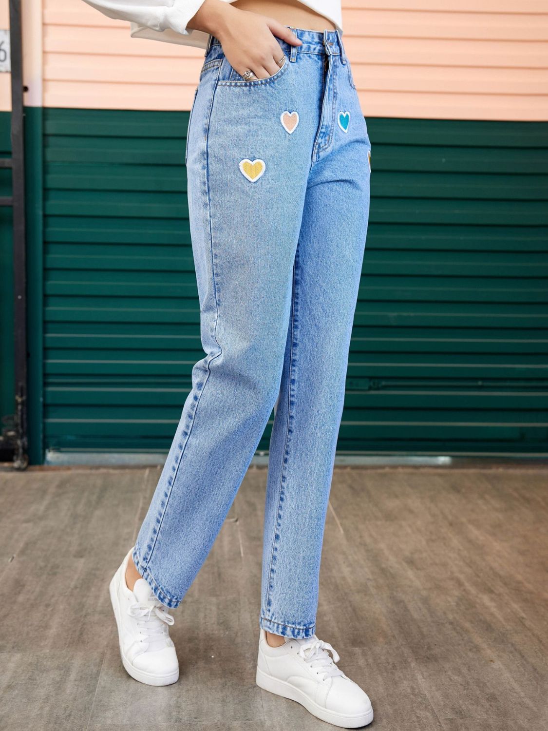 Light wash denim jeans with colorful heart patches and a straight leg cut.