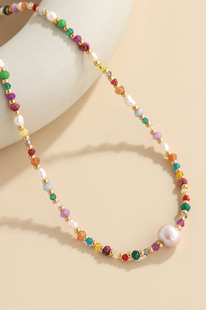 Multicolor beaded gemstone and pearl necklace with gold accents and a large pink pearl.