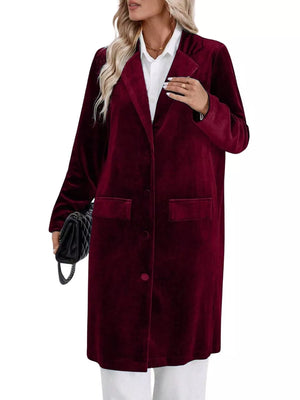 Burgundy velvet longline trench coat with lapel collar, buttoned front, and flap pockets.
