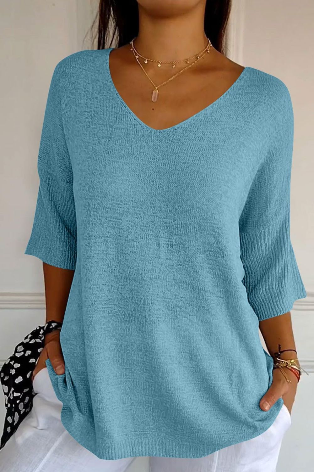 Pastel blue knit sweater with V-neck and flared sleeves, textured fabric.
