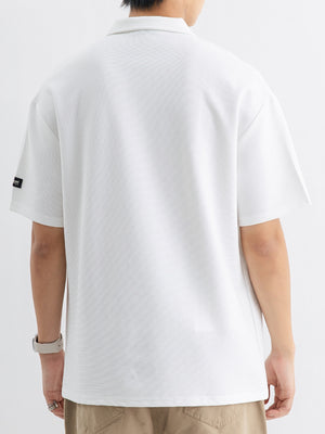 White cotton polo shirt with short sleeves and metallic accent tag on left sleeve.
