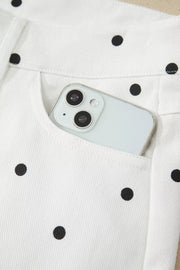 White chino shorts with black polka dots and a phone in the pocket.