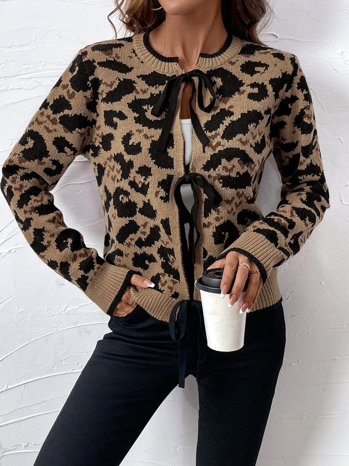Tan leopard print knit cardigan with black bow-tie closures and ribbed trim.