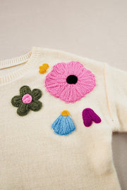 Cream knit sweater with embroidered floral appliqués in pink, green, blue, yellow, and purple.