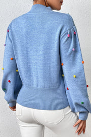 Blue blouson knit sweater with multicolor pom-pom embellishments on sleeves and shoulders.