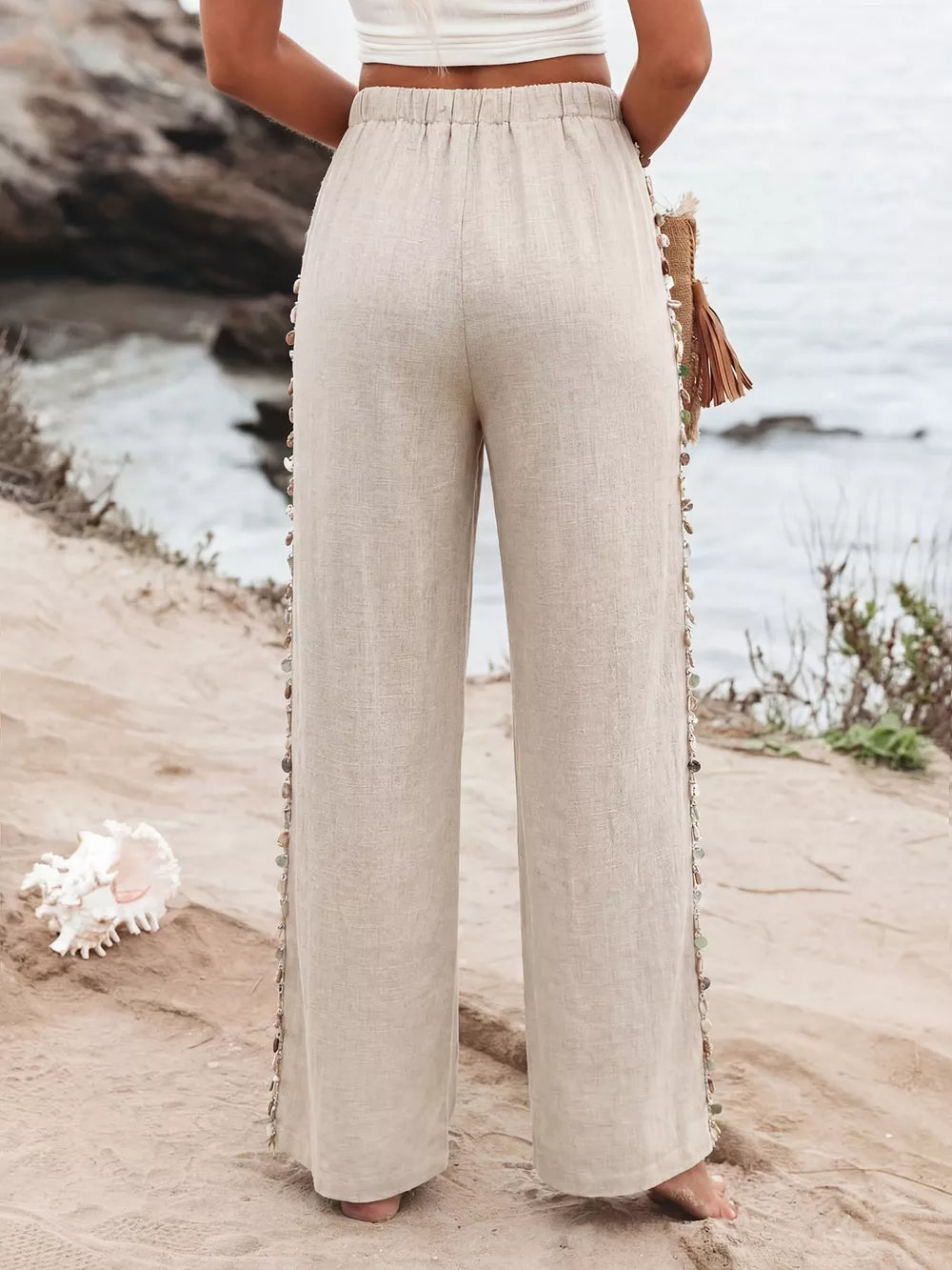 Relaxed beige linen wide-leg trousers with drawstring waist and beaded side detail.