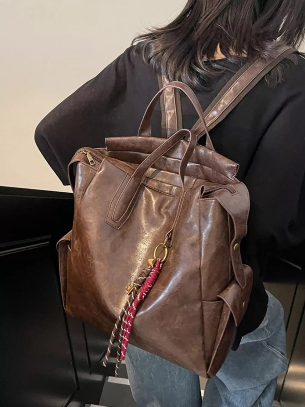 Convertible leather backpack in coffee brown with braided tassel detail and side pockets.