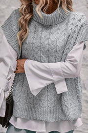 Gray cable knit turtleneck capelet sweater with ribbed trim, layered over a white shirt.