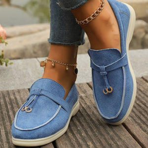 Blue suede flat slip-ons with decorative strap and gold hardware detail.