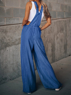 Distressed denim palazzo dungaree jumpsuit in medium wash with wide legs.