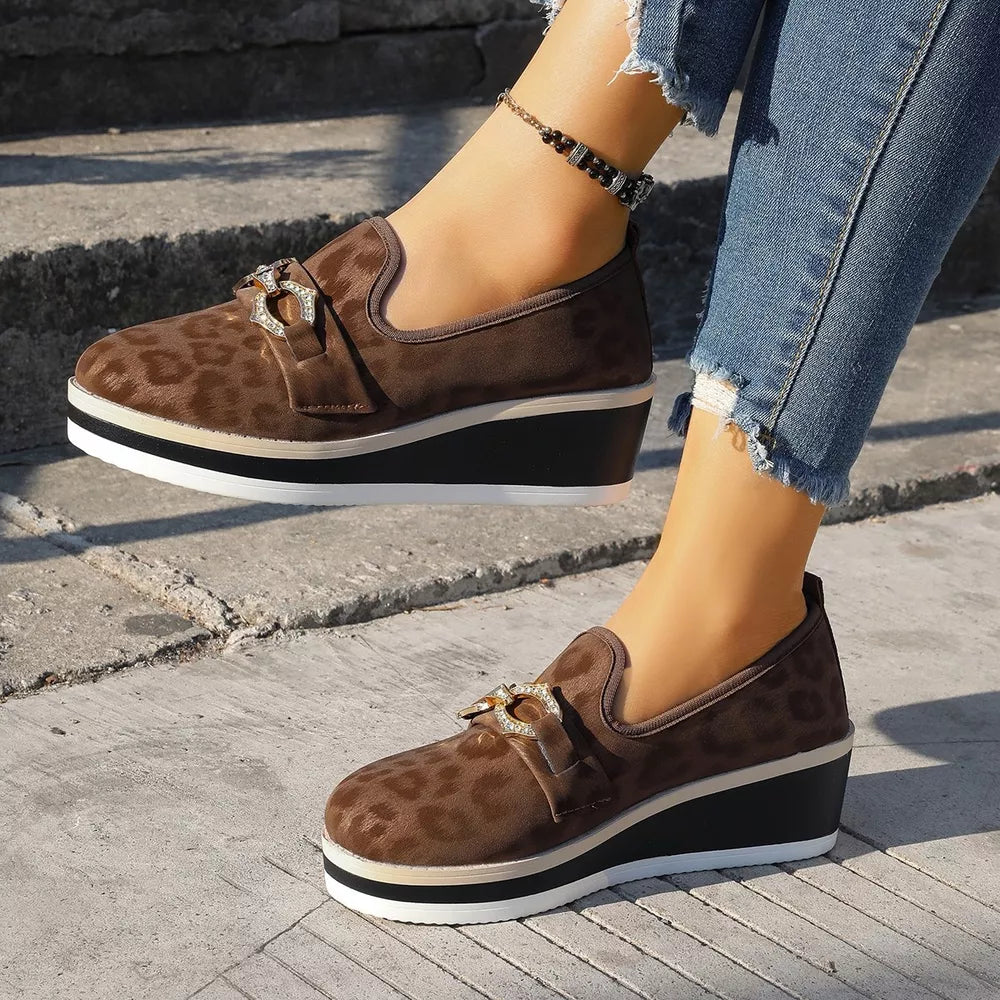Brown leopard print wedge loafers with buckle detail and layered sole.