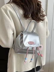 Silver leather mini drawstring backpack with beaded accents and a fluffy charm.