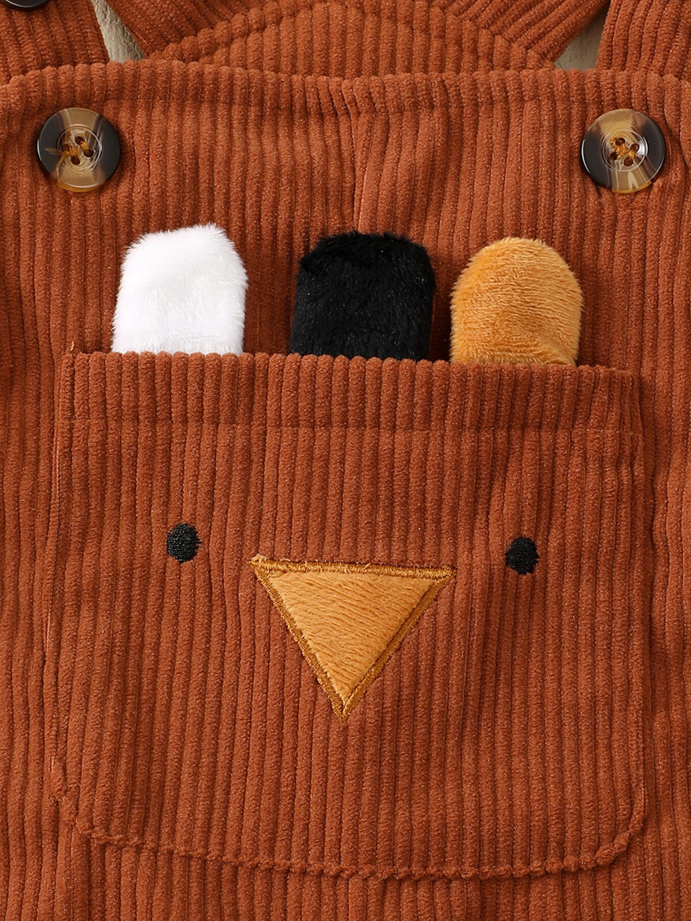 Brown corduroy overalls with bear face applique and plush ears peeking from pocket.