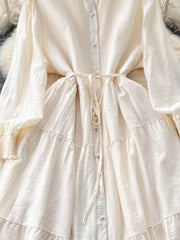 Off-white tiered long sleeve button-down dress with tie waist and textured fabric.
