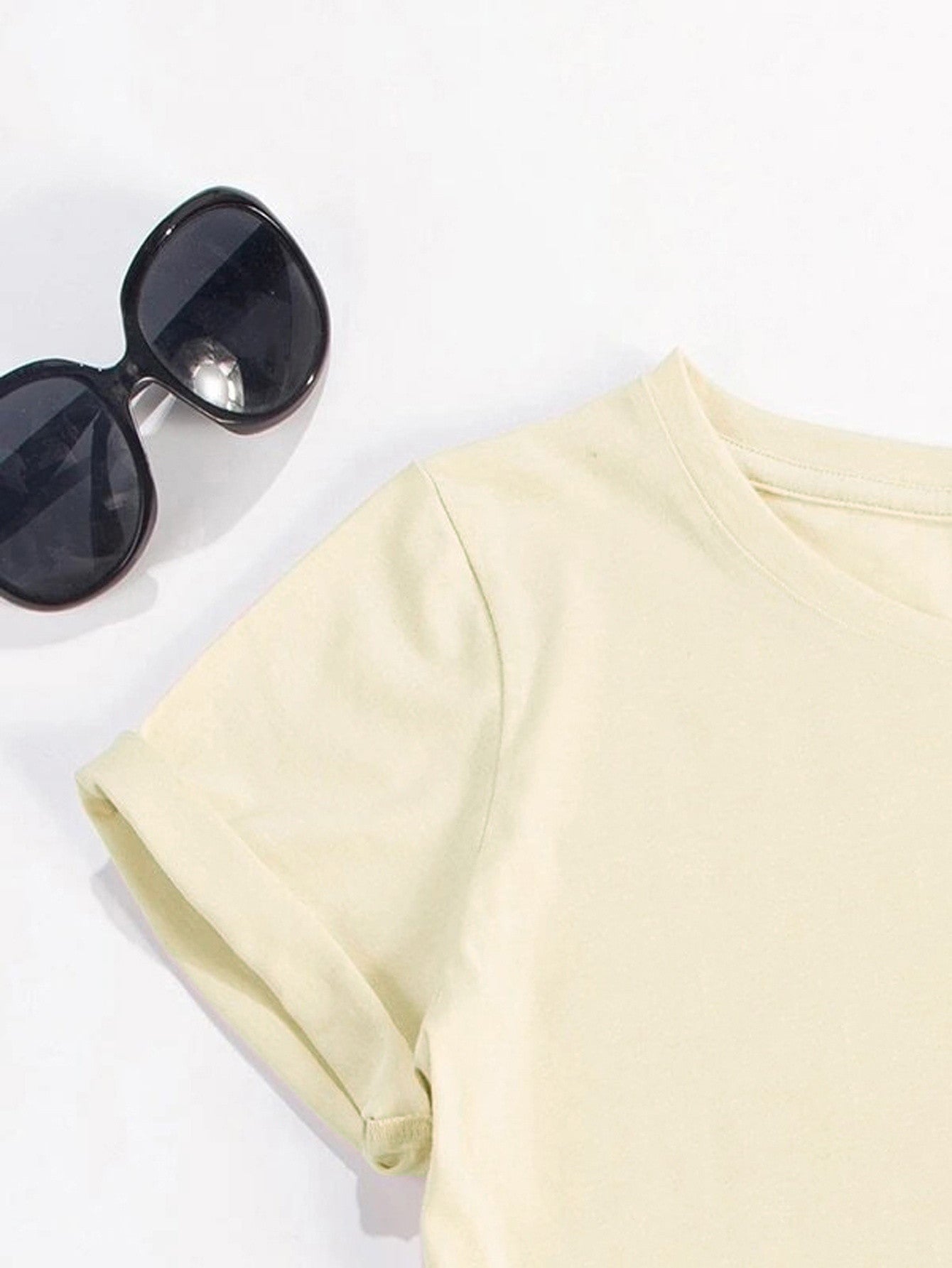 Cream graphic tee with rolled sleeves and crew neck, styled with sunglasses.