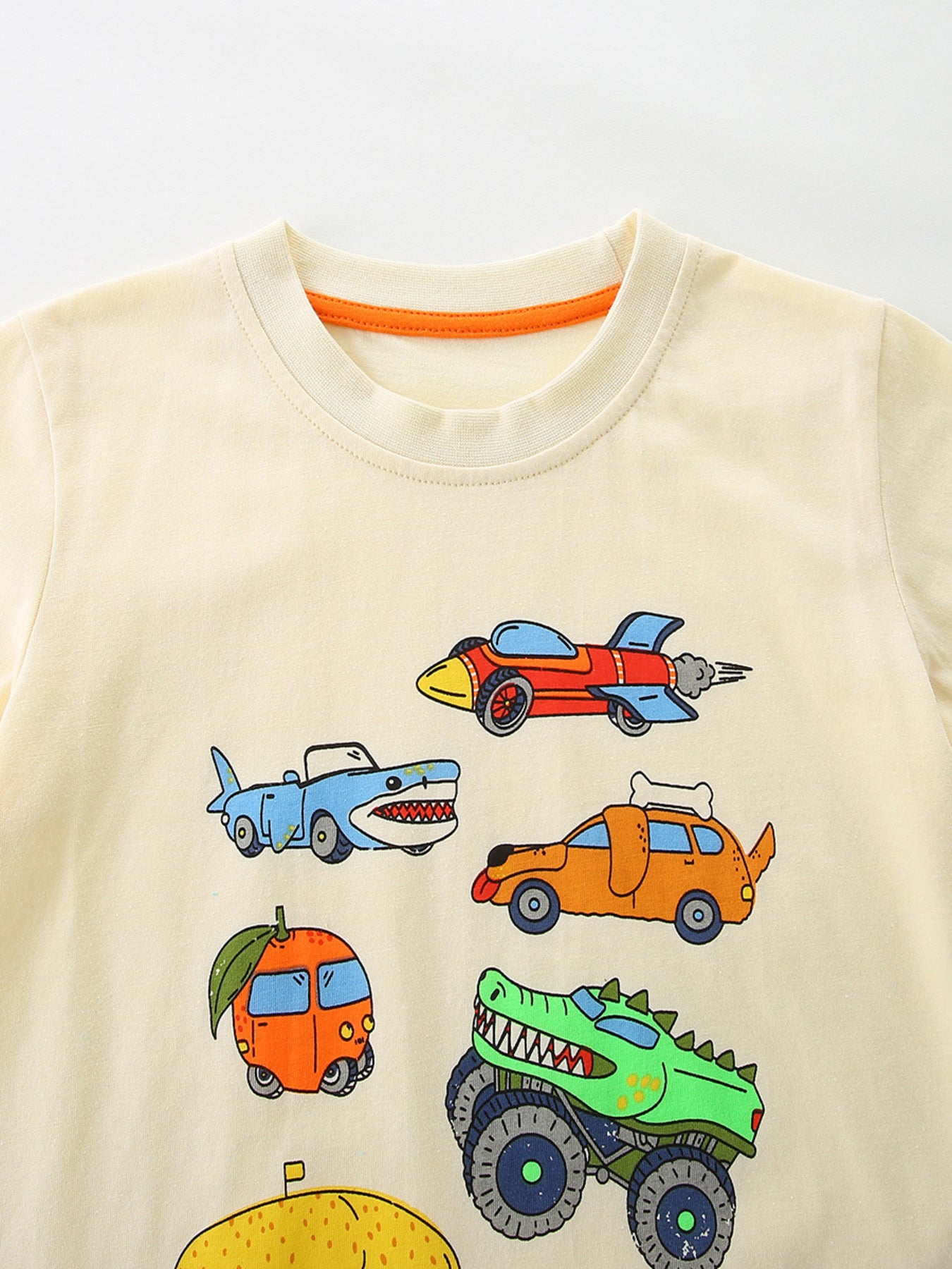 Cream cotton toddler t-shirt with whimsical vehicle print including a shark car, rocket, dog car, and monster truck.