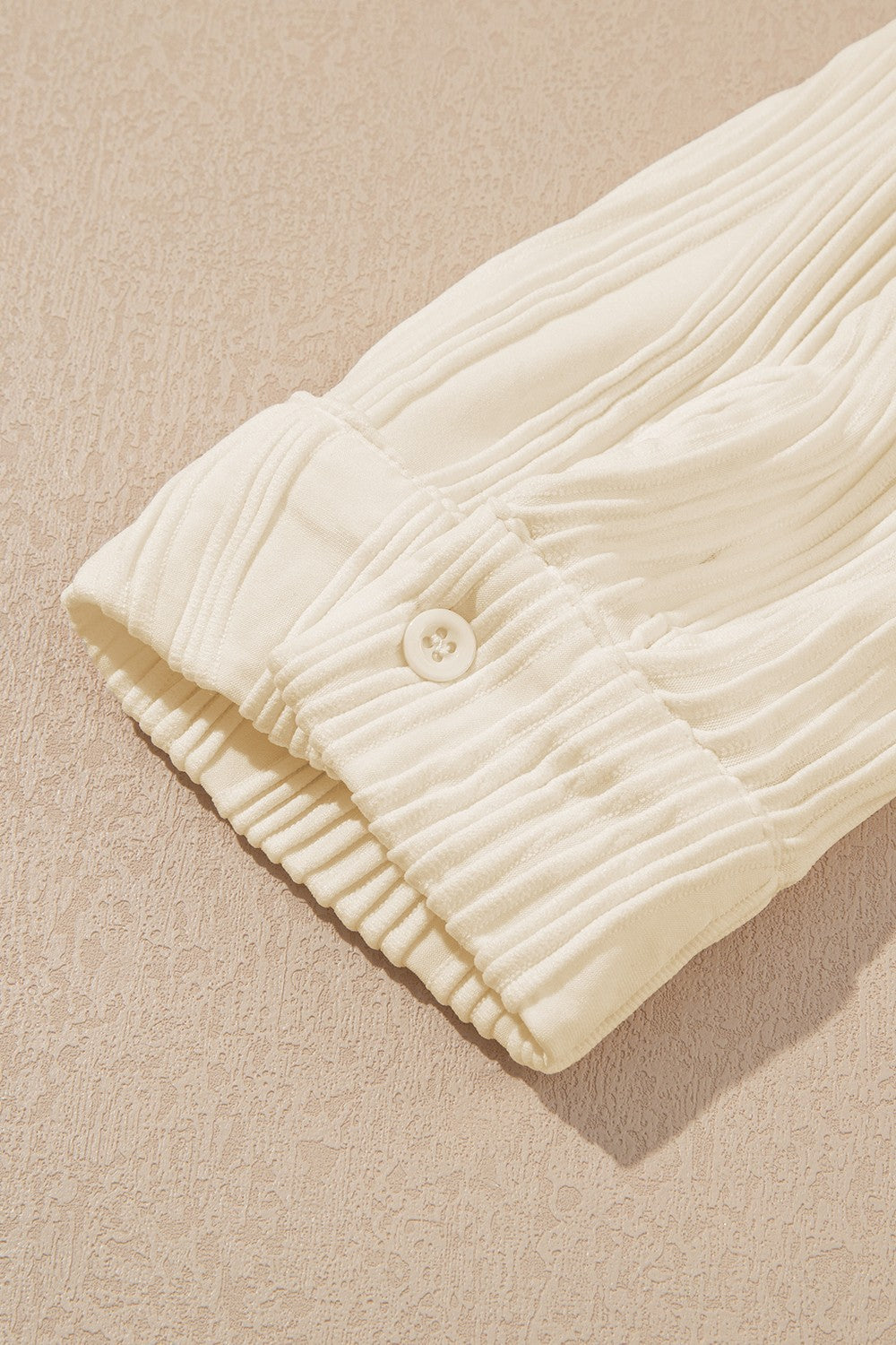 Beige oversized button-down shirt with vertical pleats and a single button cuff detail.